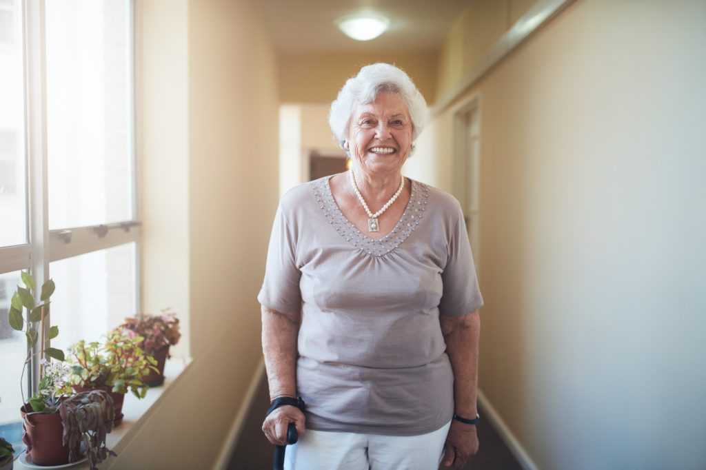 Happy senior woman with walking stick standing at home