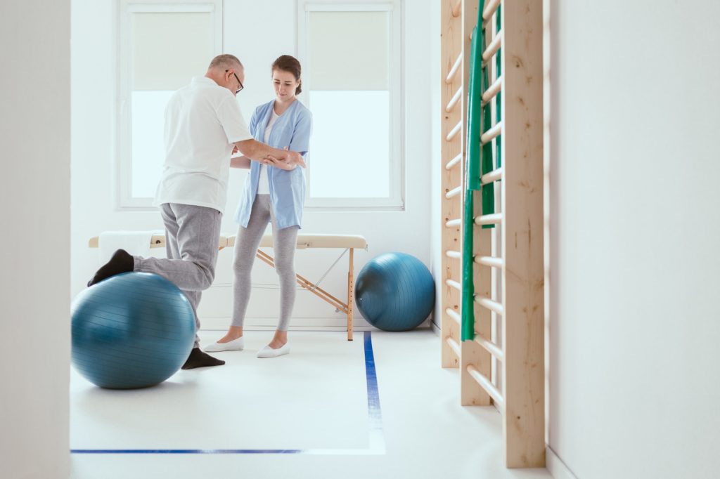 Young professional physiotherapist exercising with an injured patient using a blue ball